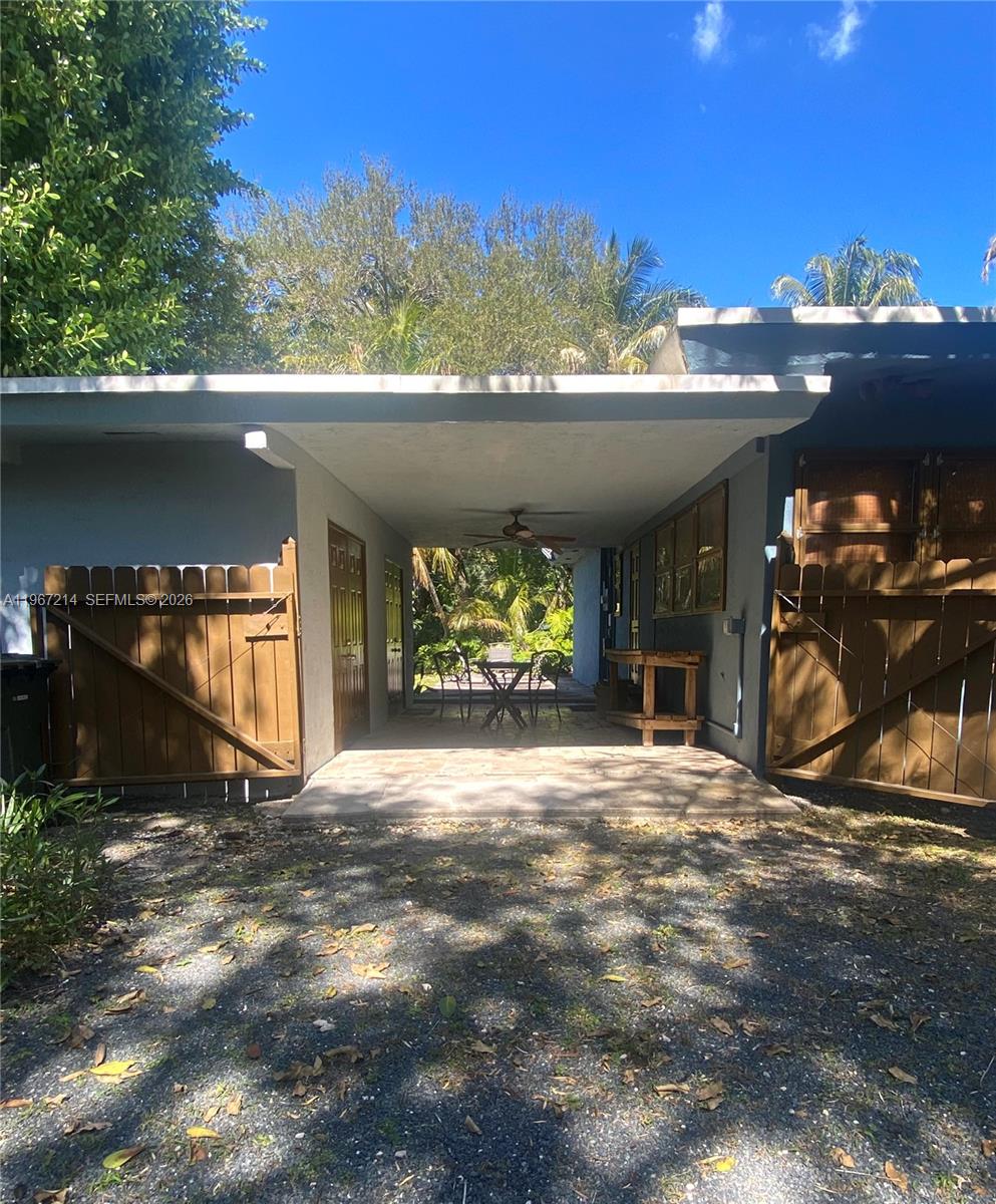 A covered patio area features a stone floor, a ceiling fan, and wooden privacy gates — 5975 SW 60th St, South Miami FL 33143, SOUTH MIAMI, FL
