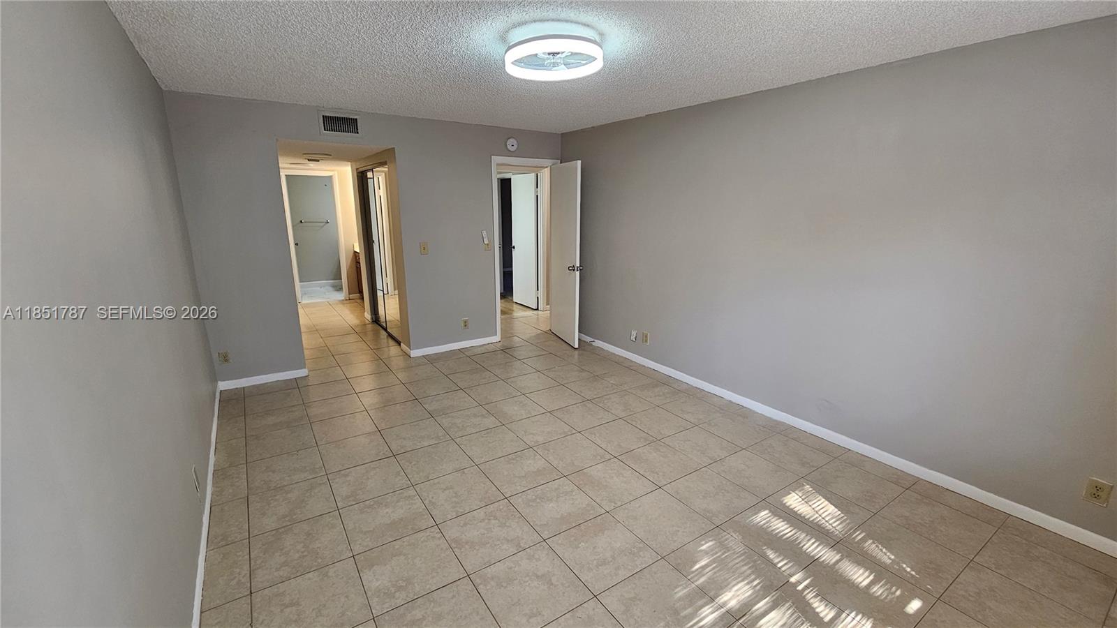 An empty room features light-colored tile flooring, gray walls, and a central ceiling light fixture — 9877 Westview Dr # 628, Coral Springs FL 33076, CORAL SPRINGS, FL