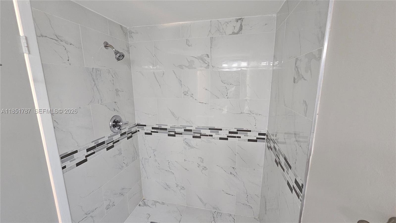 A walk-in shower features white marble-look wall tiles with a horizontal mosaic accent strip — 9877 Westview Dr # 628, Coral Springs FL 33076, CORAL SPRINGS, FL