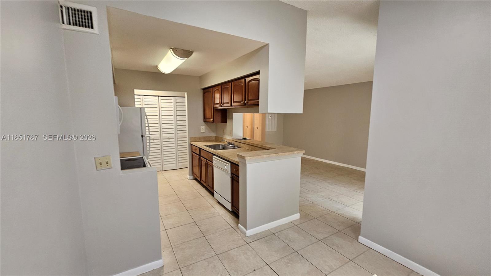 A kitchen with wood cabinets, a dishwasher, and tile flooring opens to a living area — 9877 Westview Dr # 628, Coral Springs FL 33076, CORAL SPRINGS, FL