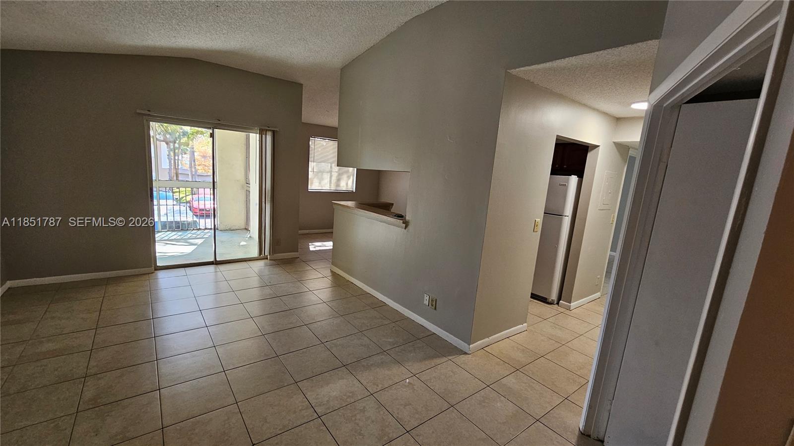 An open-concept living area features tiled floors, a pass-through kitchen window, and a sliding glass door — 9877 Westview Dr # 628, Coral Springs FL 33076, CORAL SPRINGS, FL