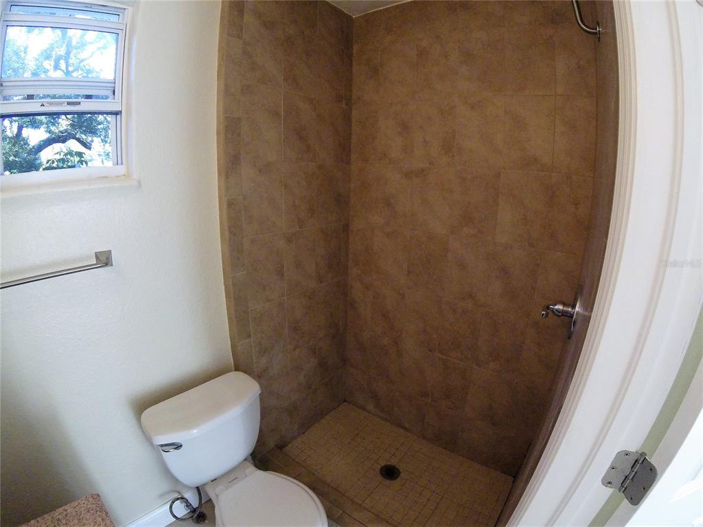 A bathroom features a tiled walk-in shower, a white toilet, and a window — 1300 28TH AVENUE N UNIT 2, ST PETERSBURG, FL