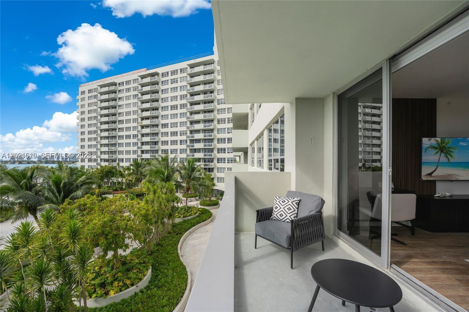 A balcony with a chair and table overlooks a landscaped courtyard and a large building — 1500 Bay Rd # 416S, Miami Beach FL 33139, MIAMI BEACH, FL