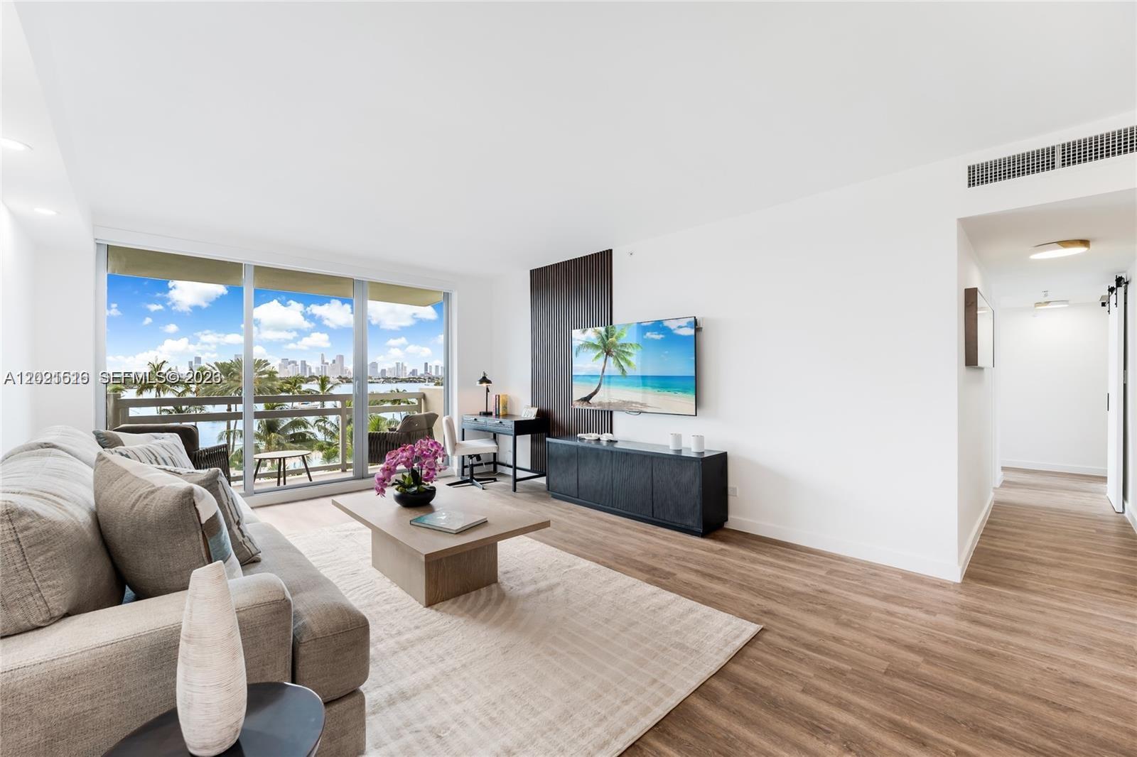 A modern living room features a sofa, television, desk, and balcony with a city view — 1500 Bay Rd # 416S, Miami Beach FL 33139, MIAMI BEACH, FL