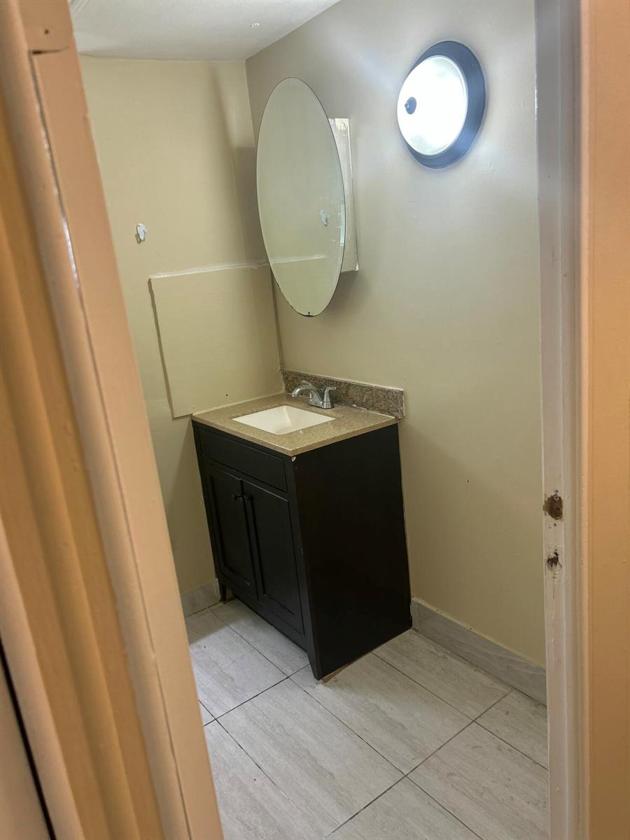 A small bathroom features a dark wood vanity, a beige countertop, and an oval mirror — 10331 Marlin Drive, Boca Raton FL 33428, BOCA RATON, FL