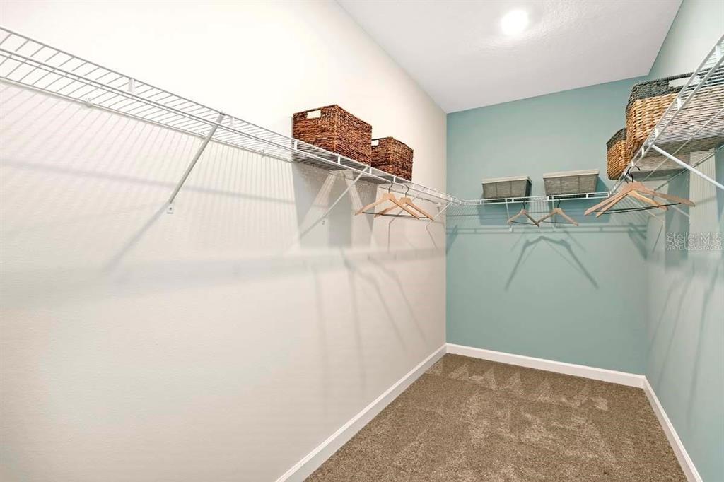 A walk-in closet features wire shelving, storage baskets, and carpeted flooring — 2519 PEACE OF MIND AVENUE, KISSIMMEE, FL