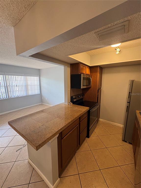 A kitchen with a tiled breakfast bar, wooden cabinets, and stainless steel appliances — 9 QUAILS RUN BOULEVARD UNIT 3, ENGLEWOOD, FL