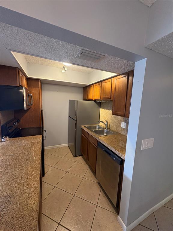 A galley kitchen features wood cabinets, granite countertops, stainless steel appliances, and tile flooring — 9 QUAILS RUN BOULEVARD UNIT 3, ENGLEWOOD, FL