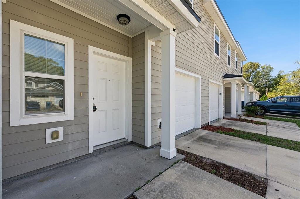 A view of a tan-sided townhouse exterior with a white front door and garage — 3551 RAIN FOREST DRIVE W, JACKSONVILLE, FL
