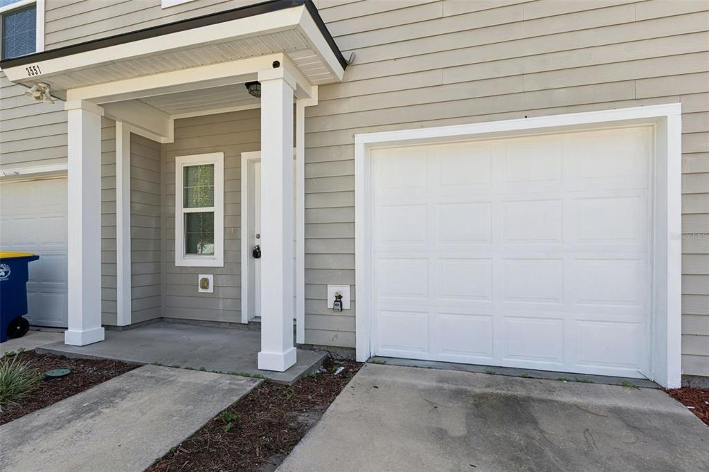 A beige townhouse exterior features a white garage door, a covered entryway, and a window — 3551 RAIN FOREST DRIVE W, JACKSONVILLE, FL