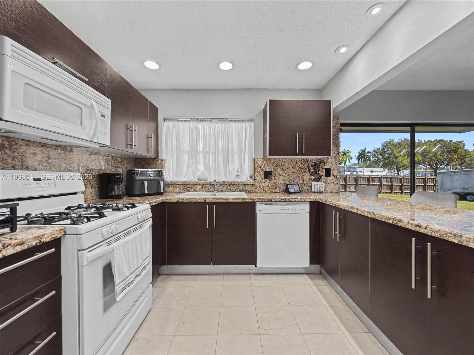 A kitchen features dark wood cabinets, granite countertops, white appliances, and a window view — 10491 SW 122nd Ct, Miami FL 33186, MIAMI, FL