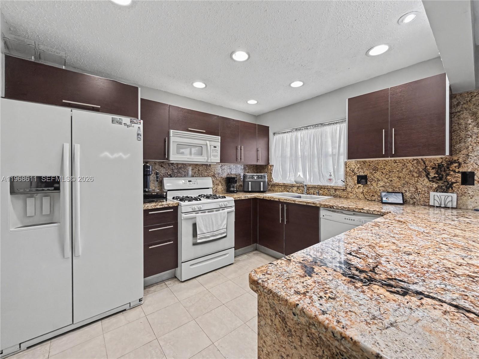 A kitchen features dark wood cabinets, granite countertops, white appliances, and recessed ceiling lighting — 10491 SW 122nd Ct, Miami FL 33186, MIAMI, FL