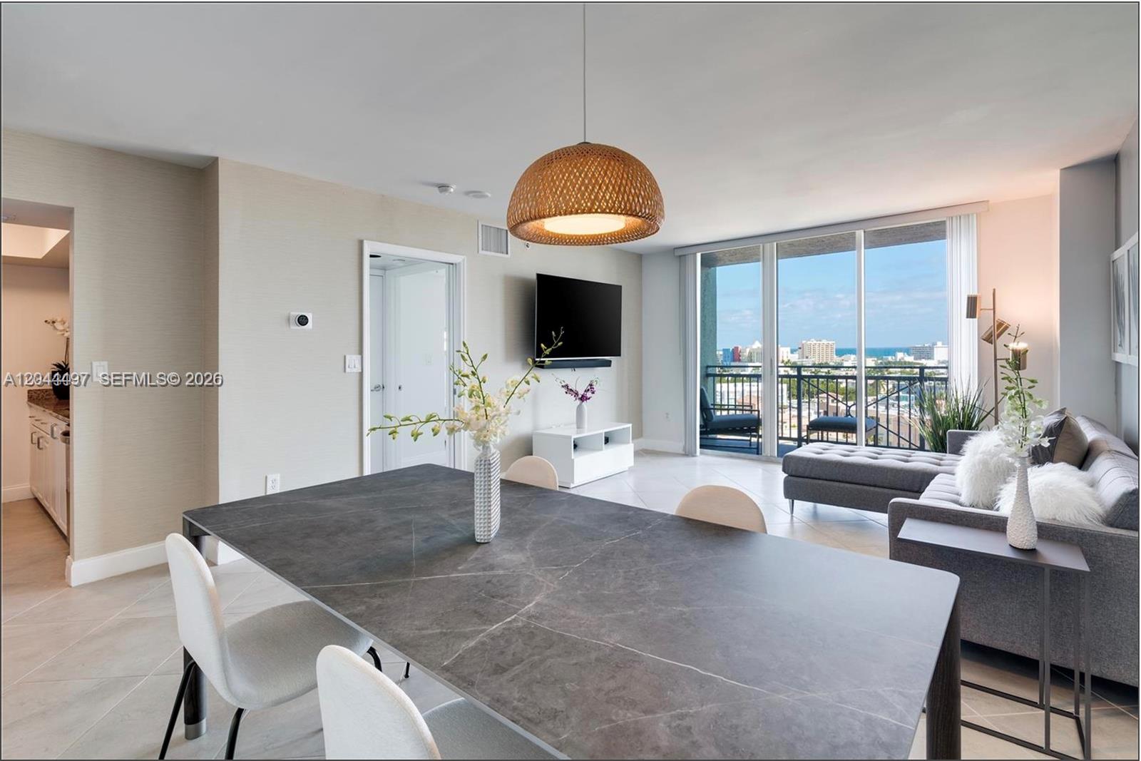A dining area with a stone table overlooks a living room with a balcony view — 90 Alton Rd # 1207, Miami Beach FL 33139, MIAMI BEACH, FL