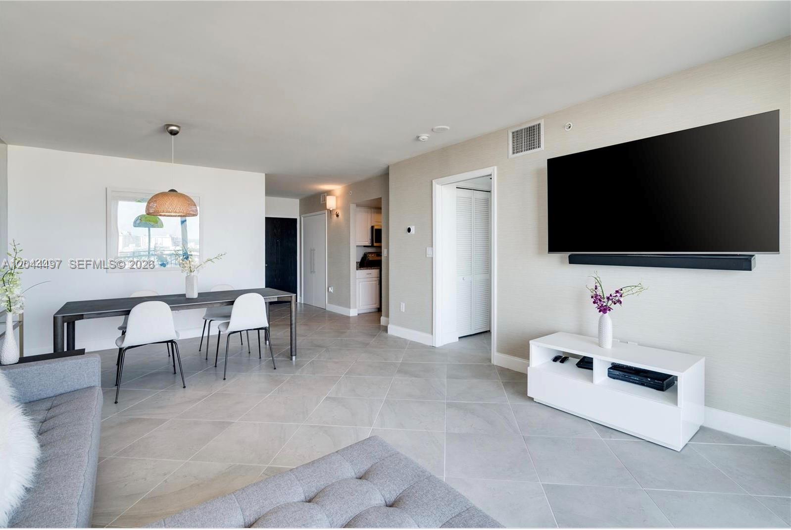 A living and dining area features light tile floors, a wall-mounted television, and modern furniture — 90 Alton Rd # 1207, Miami Beach FL 33139, MIAMI BEACH, FL