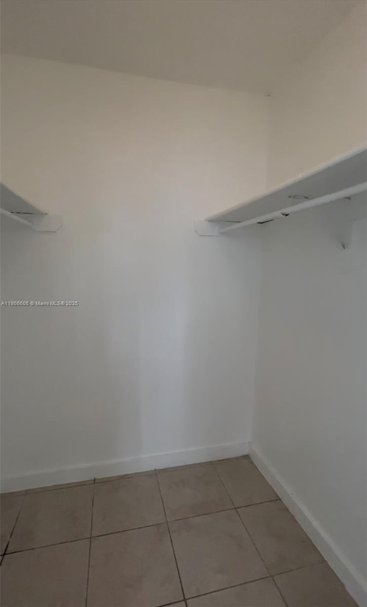 This is a small walk-in closet with white walls, tiled flooring, and built-in shelving — 498 NW 165th St Rd # 101, Miami FL 33169, MIAMI, FL