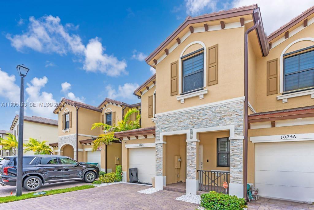 The exterior of a two-story townhouse features tan stucco walls, stone veneer accents, and a driveway — 10254 SW 228th Terrace, Miami FL 33190, MIAMI, FL