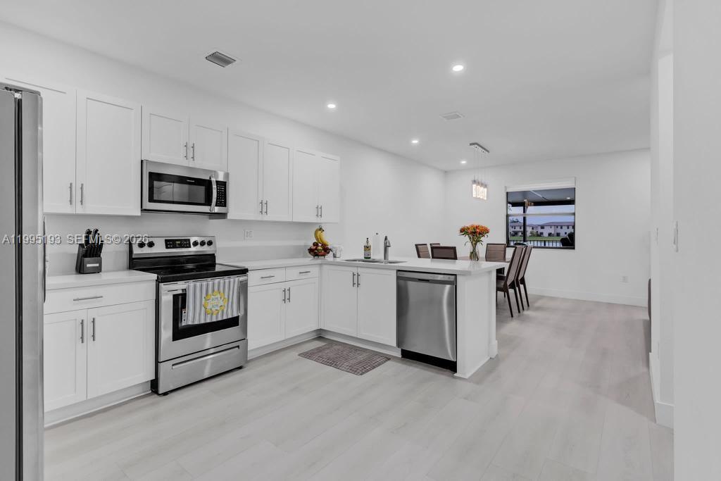 A modern kitchen features white cabinetry, stainless steel appliances, and light-colored wood-look flooring — 10254 SW 228th Terrace, Miami FL 33190, MIAMI, FL