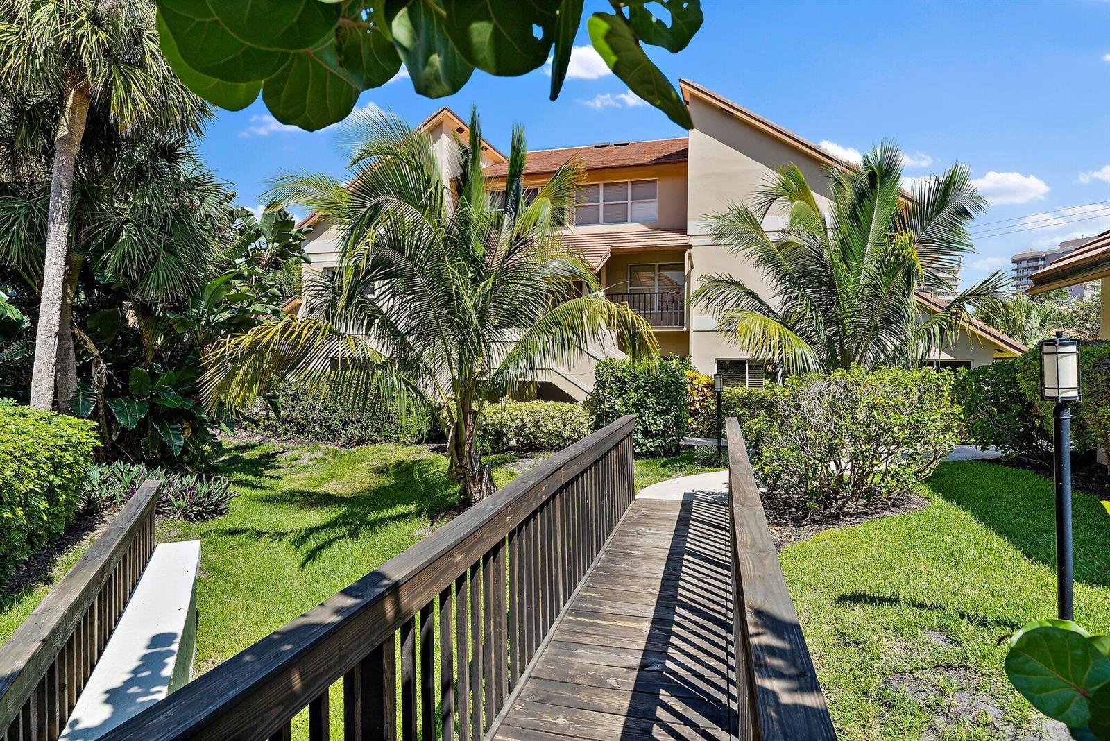 A wooden footbridge leads toward a multi-story apartment building surrounded by palm trees and landscaping — 4161 S Us Highway 1 # G3, Jupiter FL 33477, JUPITER, FL