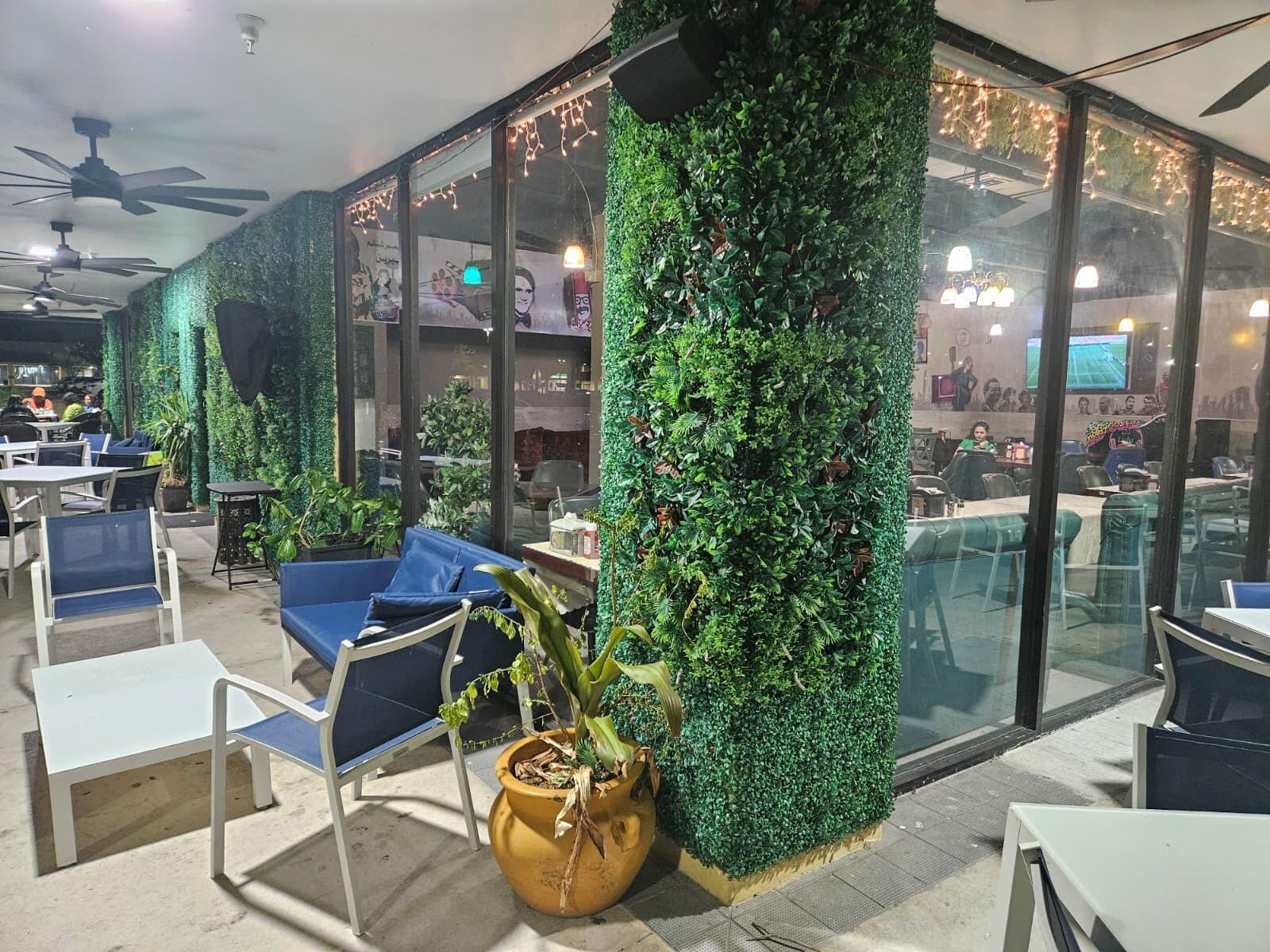 An outdoor patio area features artificial green wall panels, blue seating, and potted plants — 9050 Kimberly Boulevard # 71, Boca Raton FL 33434, BOCA RATON, FL