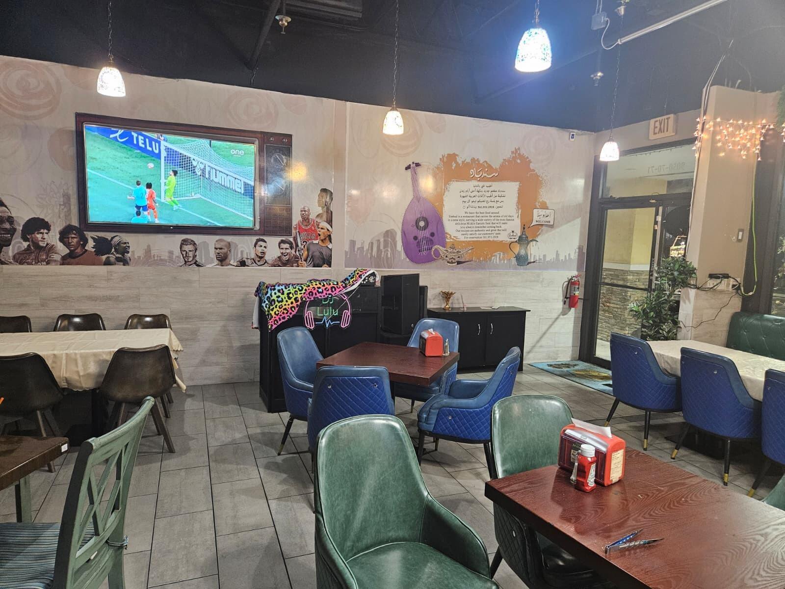 A restaurant interior features blue and green chairs, wooden tables, a television, and wall murals — 9050 Kimberly Boulevard # 71, Boca Raton FL 33434, BOCA RATON, FL