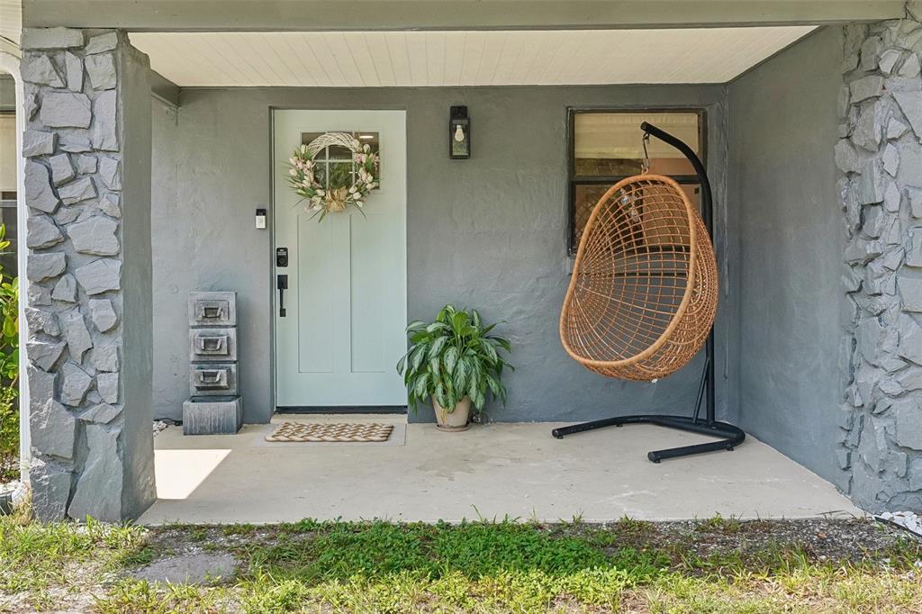 A gray exterior wall features a light blue front door, stone pillars, and a hanging chair — 2934 W ELLIS DRIVE, TAMPA, FL