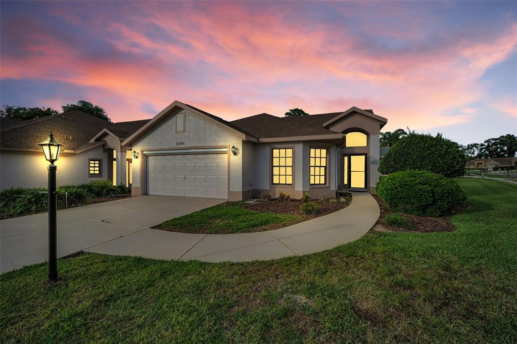 A single-story house with a two-car garage and a curved walkway at sunset — 6240 FAIRSKIES DRIVE, NEW PORT RICHEY, FL