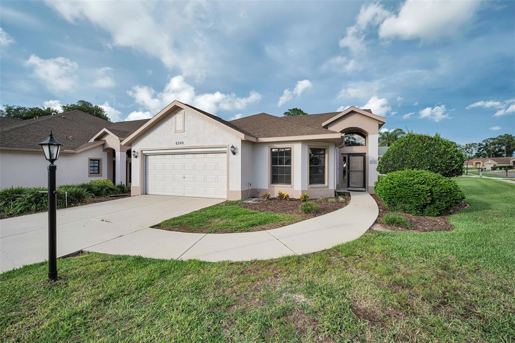 A single-story house with a beige stucco exterior, a two-car garage, and a concrete driveway — 6240 FAIRSKIES DRIVE, NEW PORT RICHEY, FL