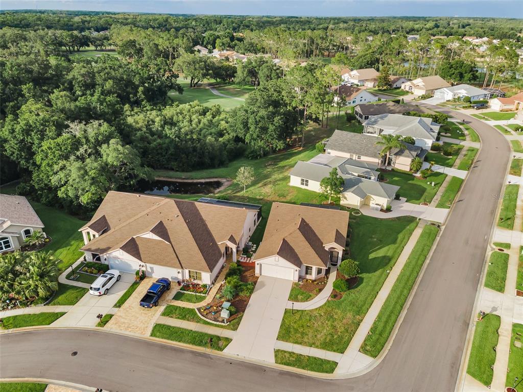 An aerial view shows two adjacent suburban houses with brown roofs and driveways near a pond — 6240 FAIRSKIES DRIVE, NEW PORT RICHEY, FL