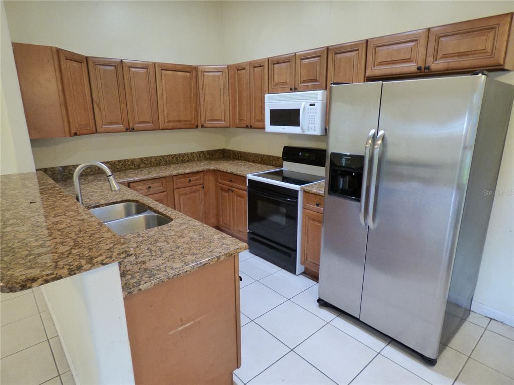 A kitchen features wood cabinets, granite countertops, a stainless steel refrigerator, and a black stove — 3122 LORRY LANE, ORLANDO, FL