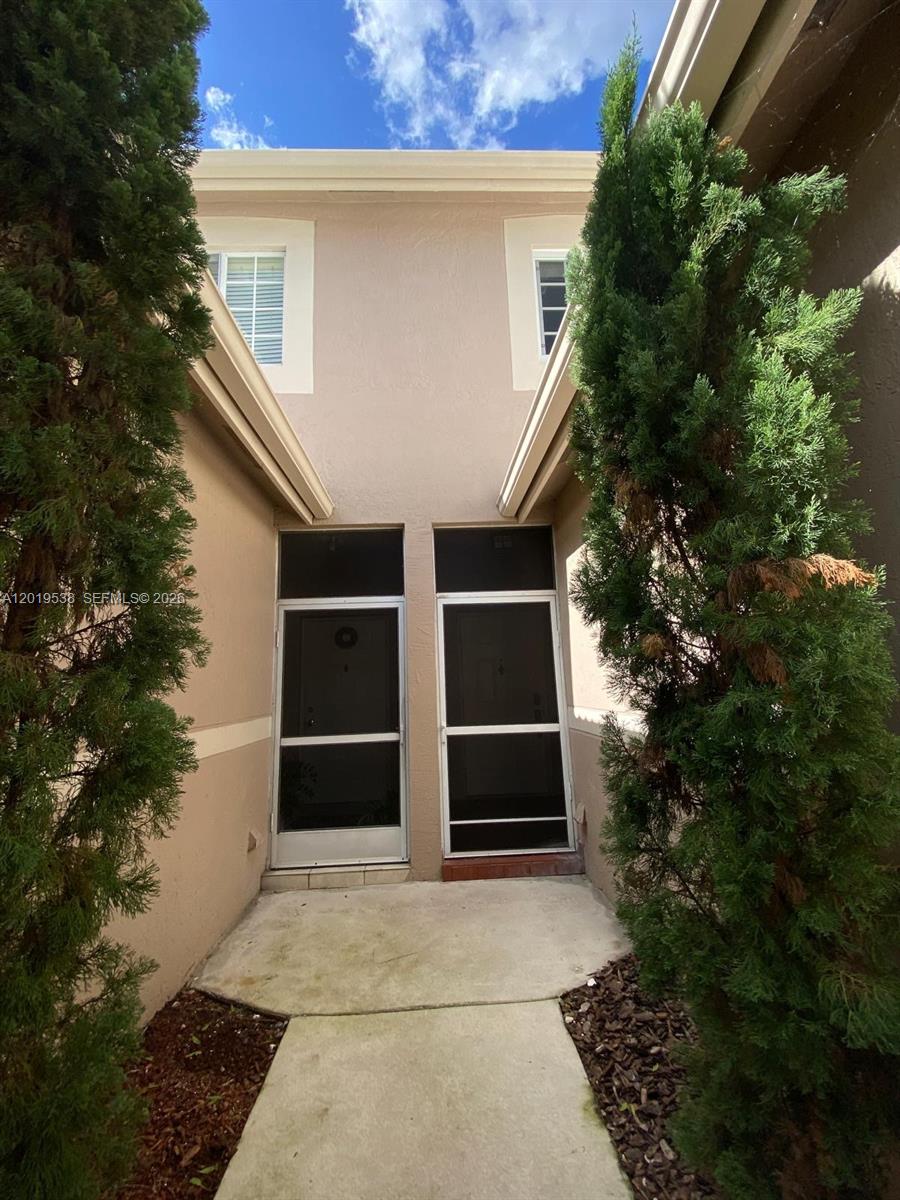 A concrete walkway leads to two screened entry doors framed by tall evergreen trees — 2041 Pompeii Ct # 2014, Weston FL 33327, WESTON, FL