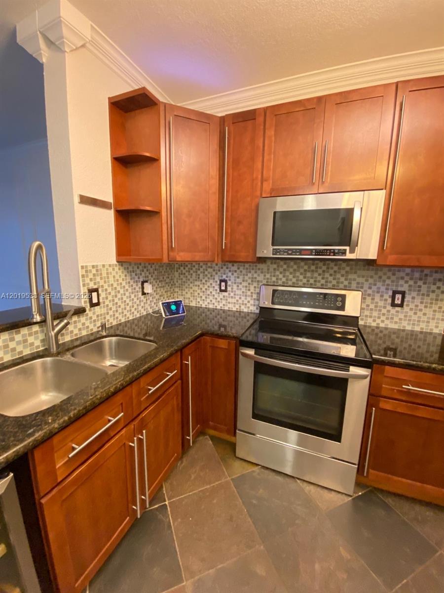 A kitchen features dark wood cabinets, granite countertops, stainless steel appliances, and a tiled backsplash — 2041 Pompeii Ct # 2014, Weston FL 33327, WESTON, FL