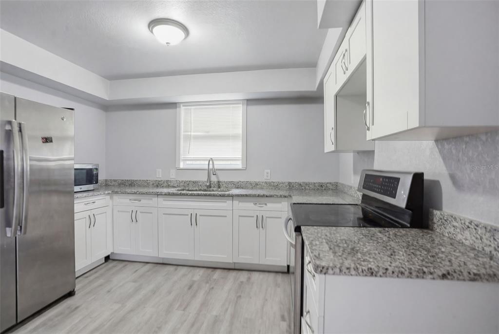 A kitchen features white cabinets, granite countertops, stainless steel appliances, and light wood-look flooring — 13379 CHAMBORD STREET, BROOKSVILLE, FL