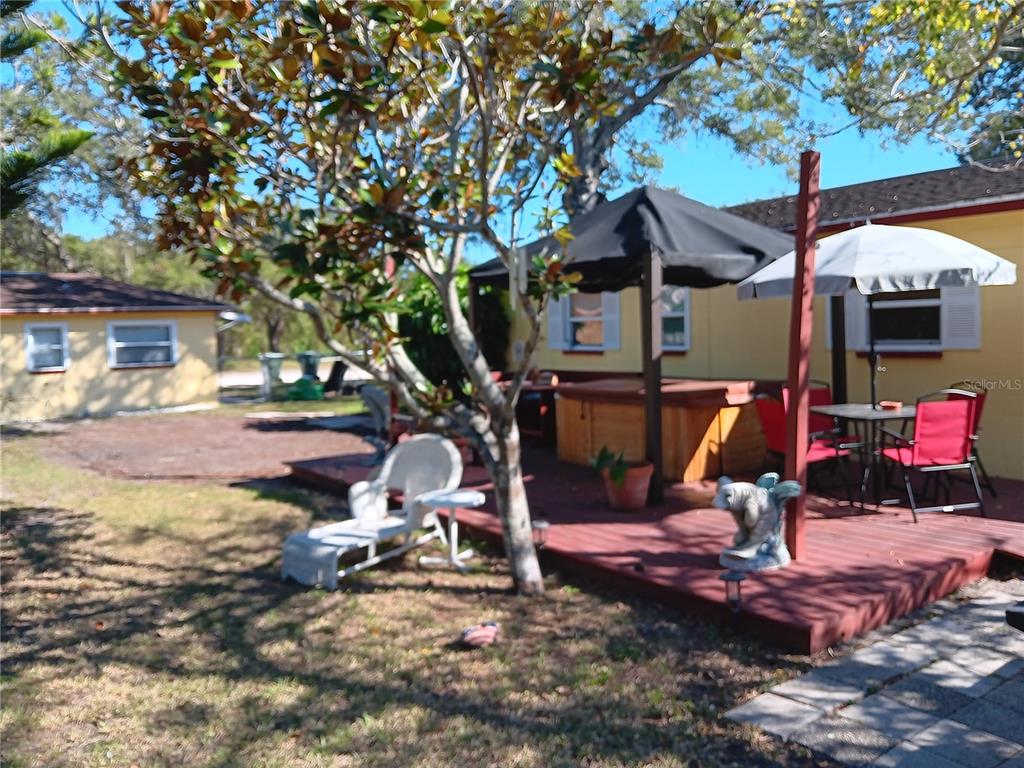 A wooden deck features a hot tub, patio furniture, and a large umbrella under trees — 374 3RD STREET NW, LARGO, FL