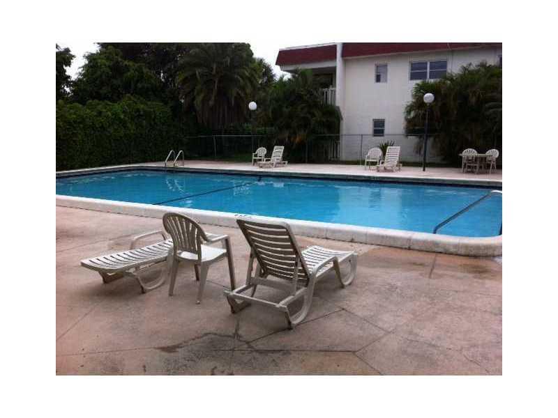 A rectangular swimming pool sits on a concrete patio with lounge chairs and a building — 4165 SW 67th Avenue # 107b, Davie FL 33314, DAVIE, FL