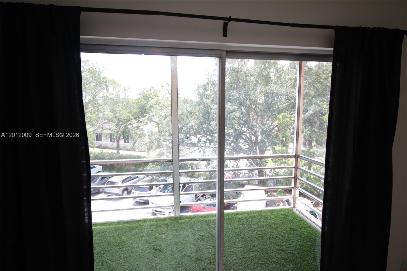 A balcony with artificial turf and a screened enclosure overlooks a parking lot — 4314 NW 9th Ave # 3C, Deerfield Beach FL 33064, DEERFIELD BEACH, FL
