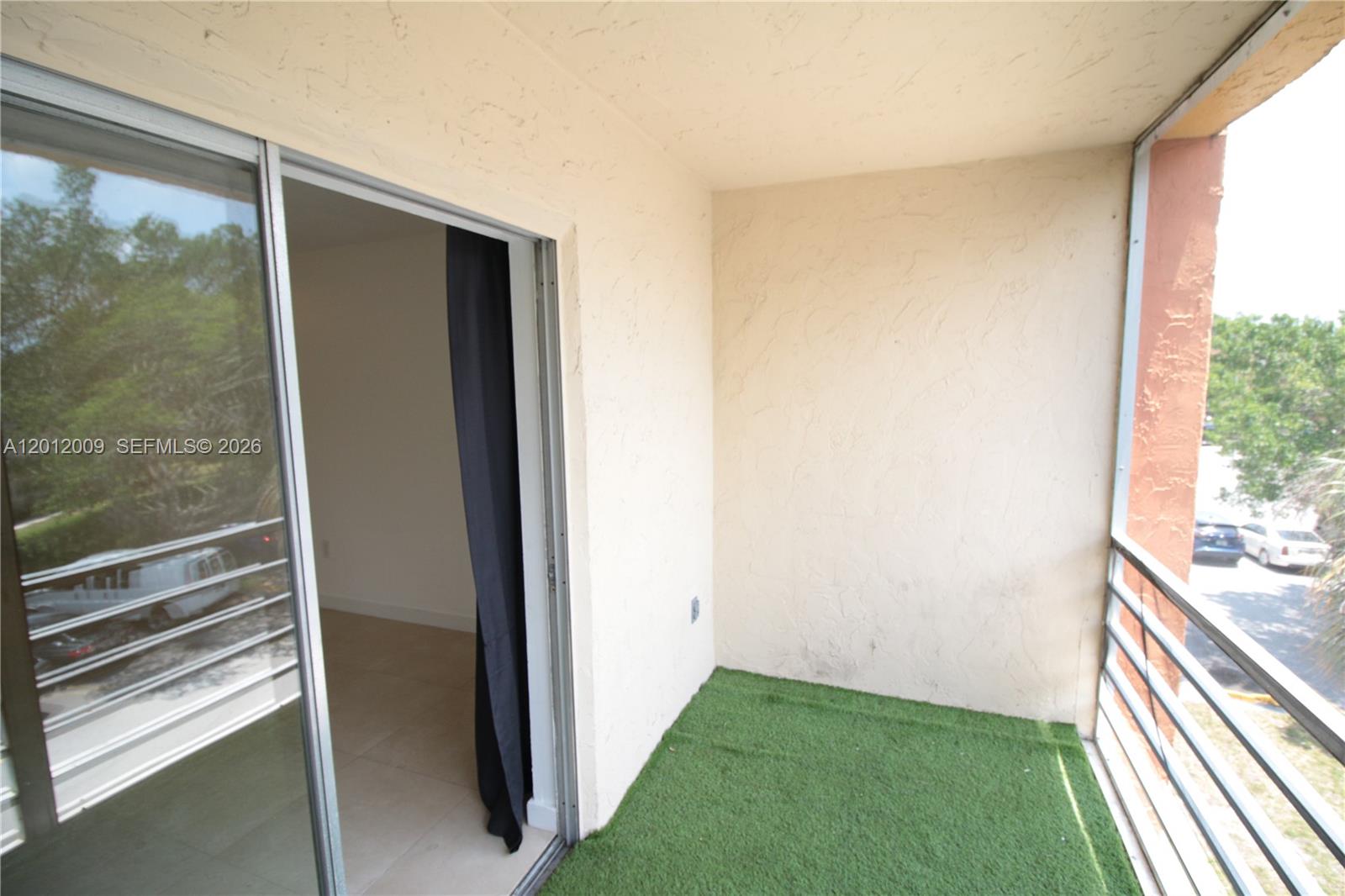 A balcony with artificial turf flooring, a sliding glass door, and metal railings — 4314 NW 9th Ave # 3C, Deerfield Beach FL 33064, DEERFIELD BEACH, FL