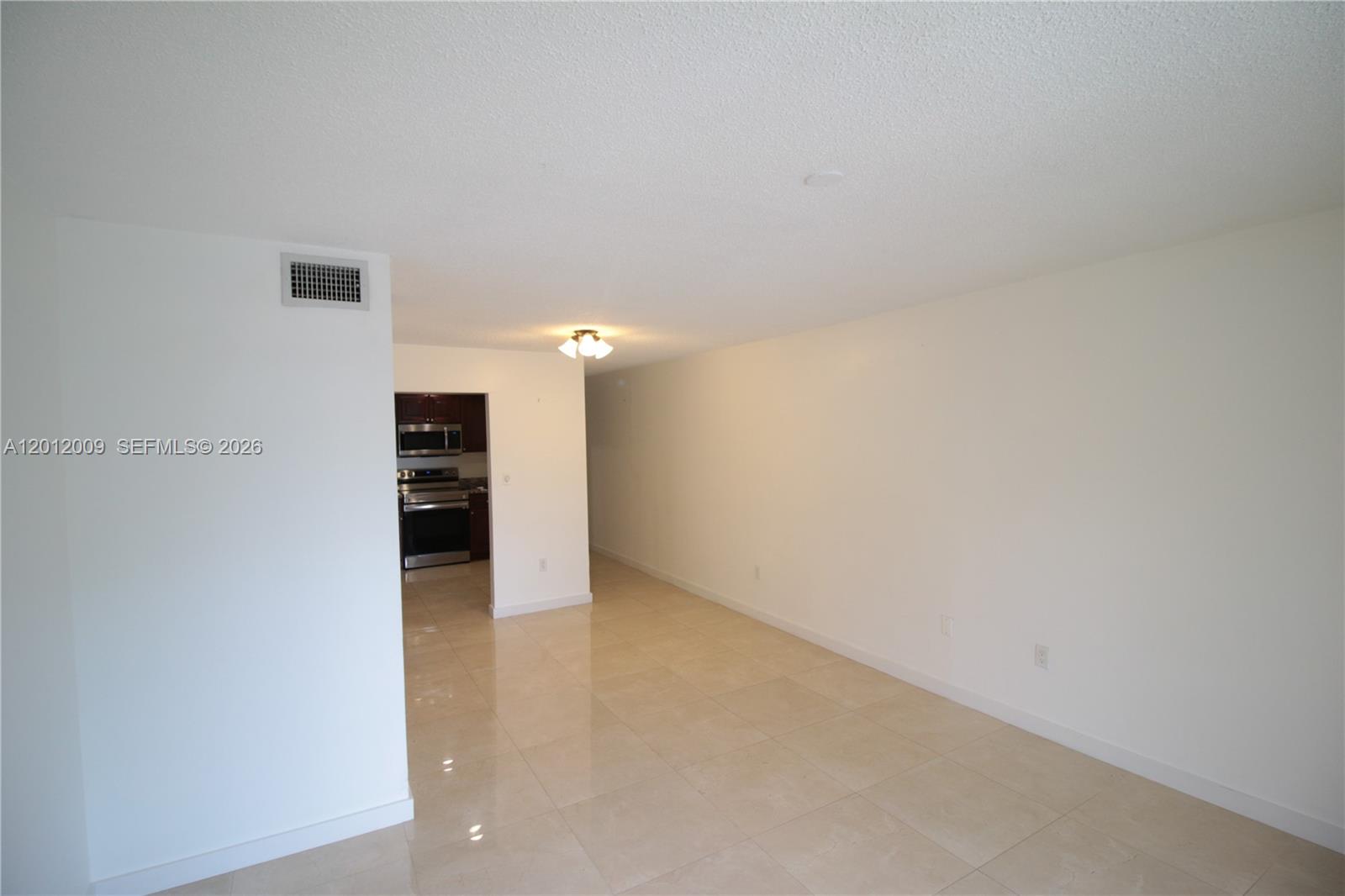 An empty room with light-colored tile floors leads to a kitchen with dark cabinets — 4314 NW 9th Ave # 3C, Deerfield Beach FL 33064, DEERFIELD BEACH, FL