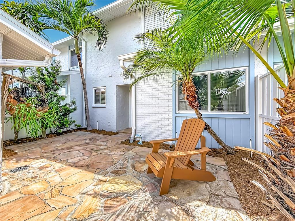 A stone patio features a wooden Adirondack chair in front of a white brick building — 6537 CAPE HATTERAS WAY NE UNIT 2, ST PETERSBURG, FL