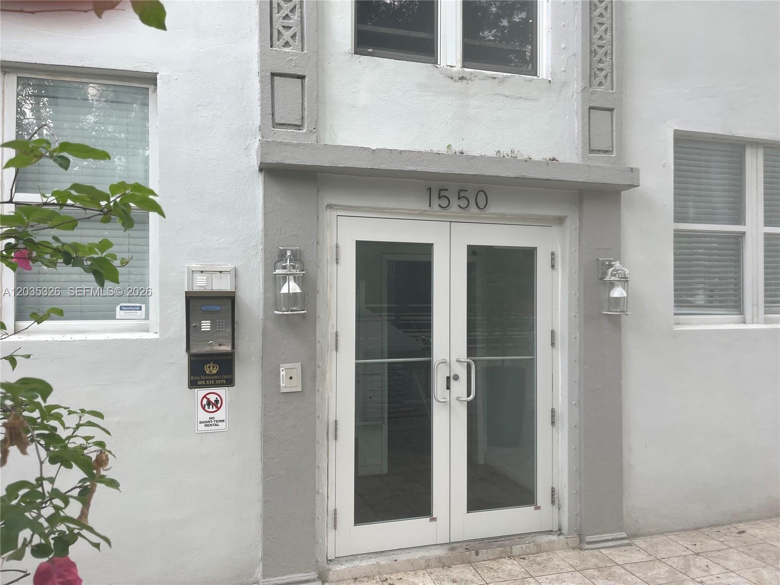 The exterior entrance of a building features double glass doors, wall-mounted lanterns, and a keypad — 1550 Drexel Ave # 203, Miami Beach FL 33139, MIAMI BEACH, FL