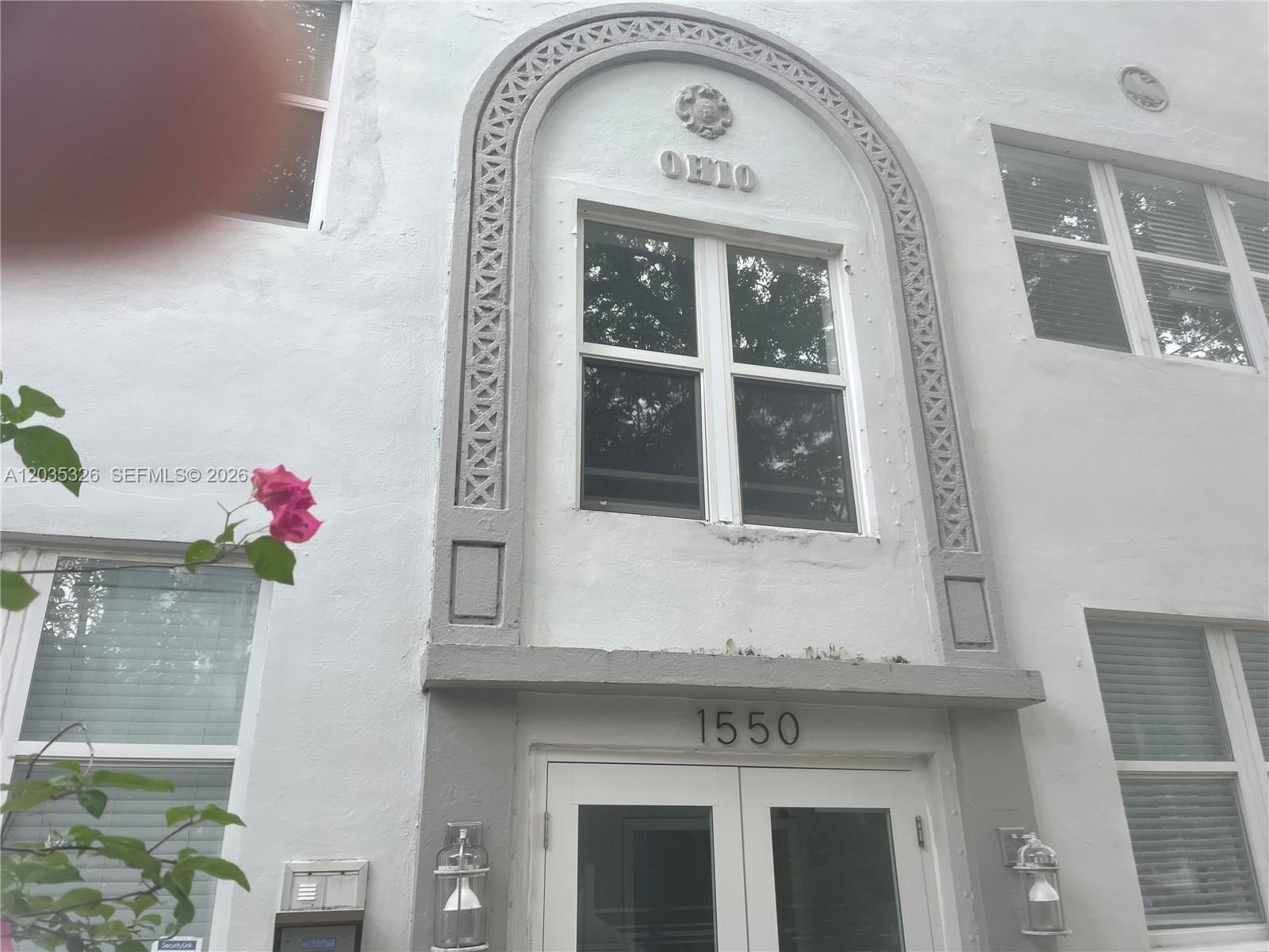 The exterior of a white building features an arched entryway with decorative molding and windows — 1550 Drexel Ave # 203, Miami Beach FL 33139, MIAMI BEACH, FL