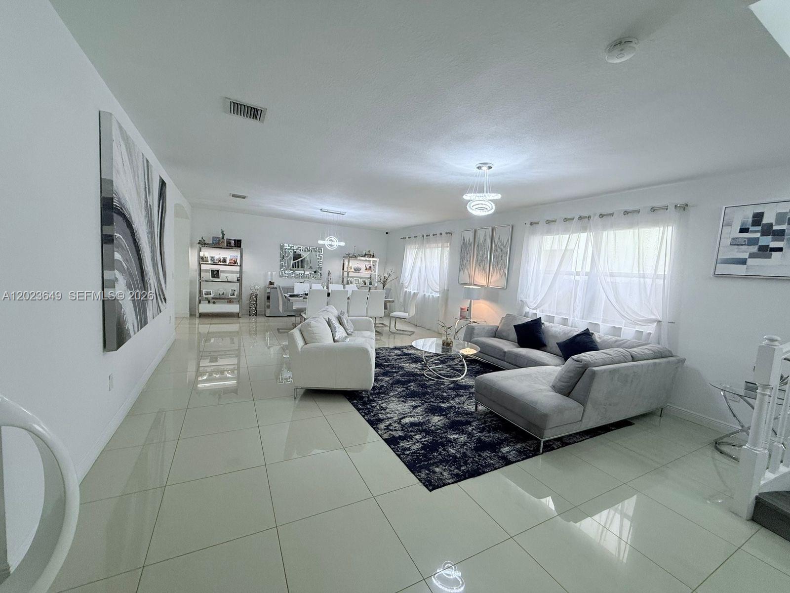 A bright, open-concept living and dining area features white tile floors and modern gray furniture — 9907 NW 87th Ter, Doral FL 33178, DORAL, FL