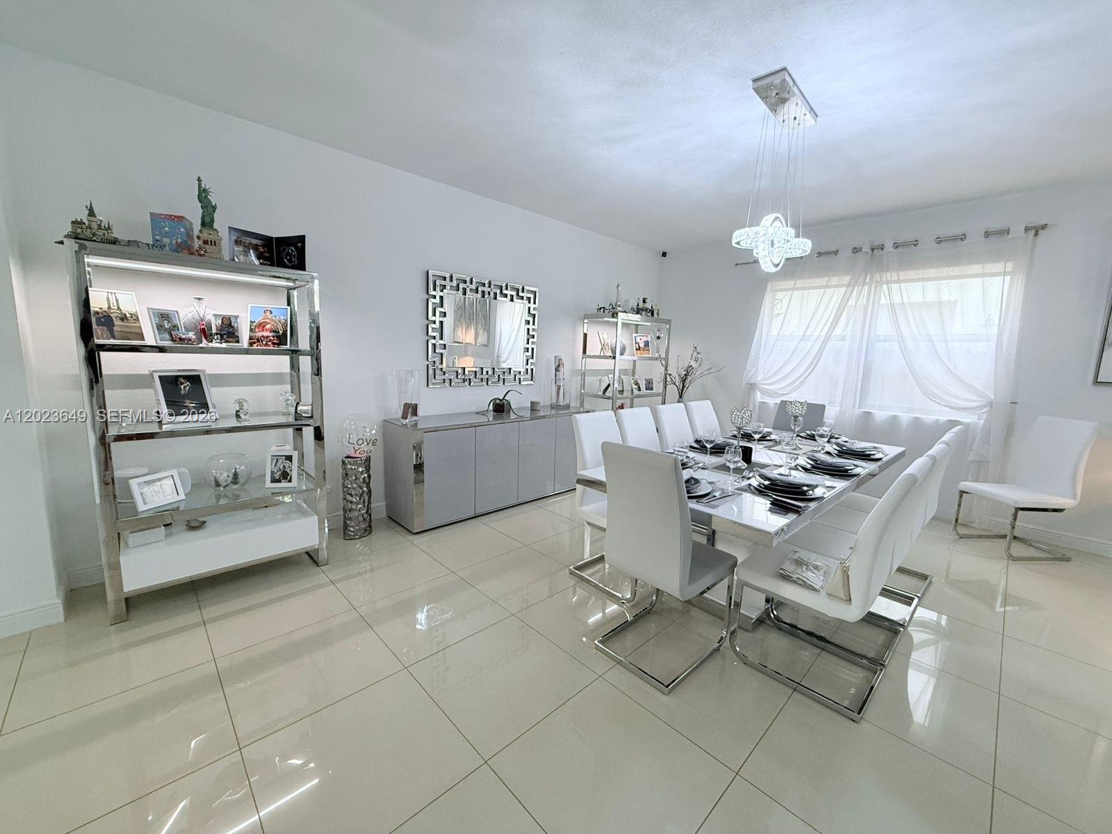A modern dining room features white furniture, a glass table, and a contemporary chandelier — 9907 NW 87th Ter, Doral FL 33178, DORAL, FL