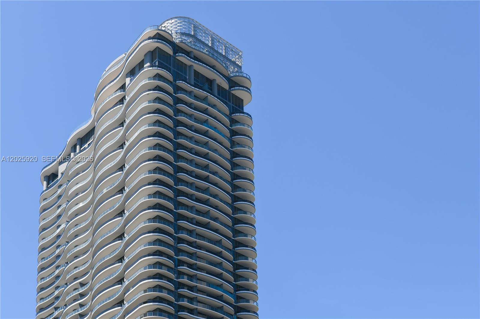A low-angle view of a modern high-rise residential building with curved balconies against a sky — 1000 Brickell # 2014, Miami FL 33131, MIAMI, FL
