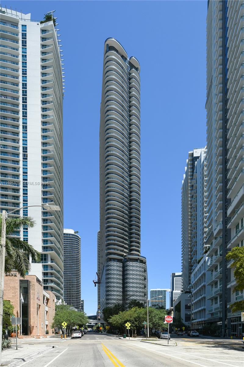 A tall, modern residential skyscraper stands between two other high-rise buildings on a city street — 1000 Brickell # 2014, Miami FL 33131, MIAMI, FL
