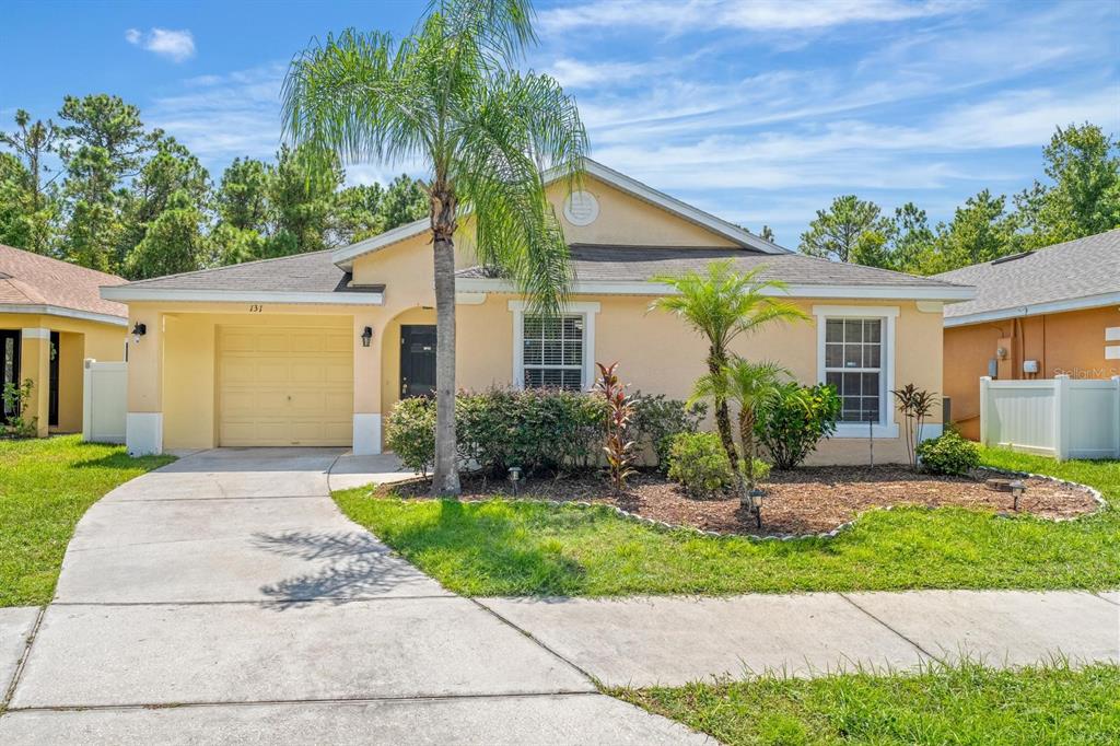 A single-story yellow house with a garage, palm trees, and a concrete driveway — 131 SANDY RIDGE DRIVE, DAVENPORT, FL