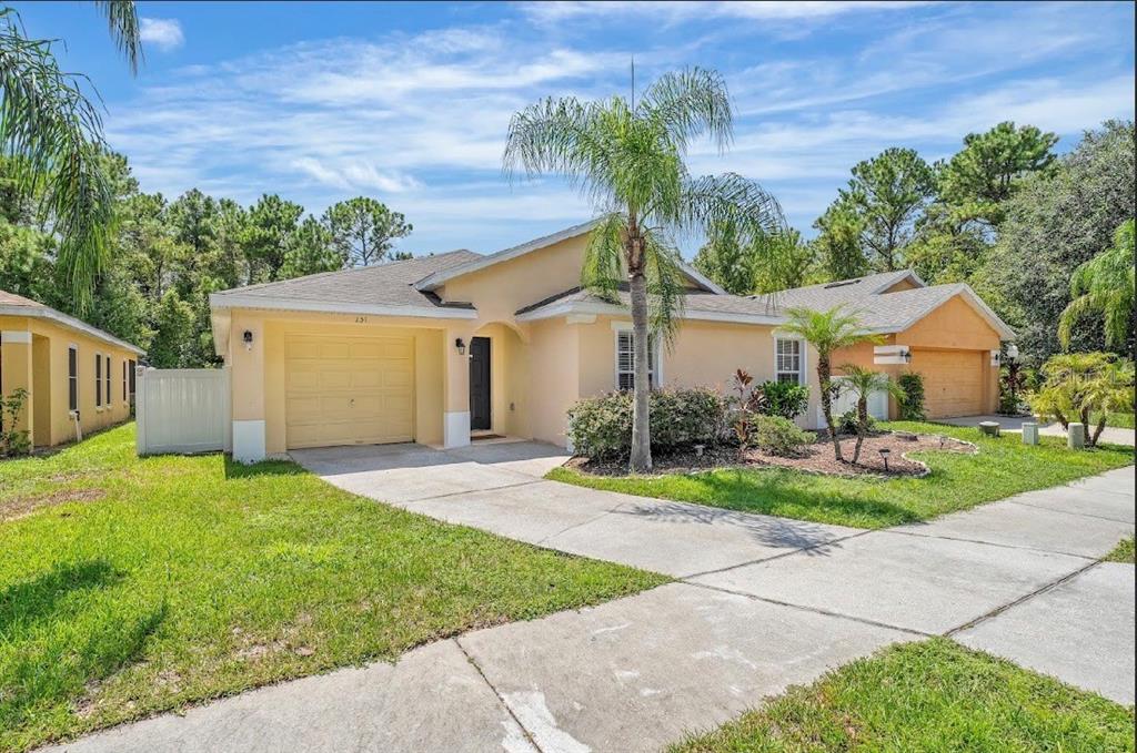 A single-story tan house with a one-car garage, a concrete driveway, and a palm tree — 131 SANDY RIDGE DRIVE, DAVENPORT, FL