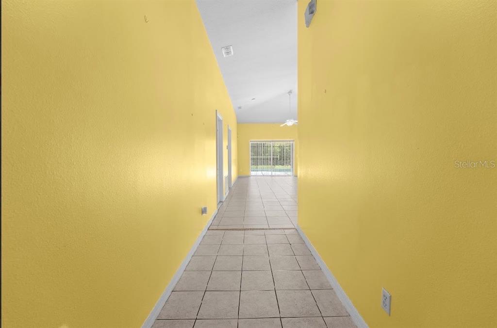 A hallway with bright yellow walls and light-colored tile flooring leads toward a sliding glass door — 131 SANDY RIDGE DRIVE, DAVENPORT, FL