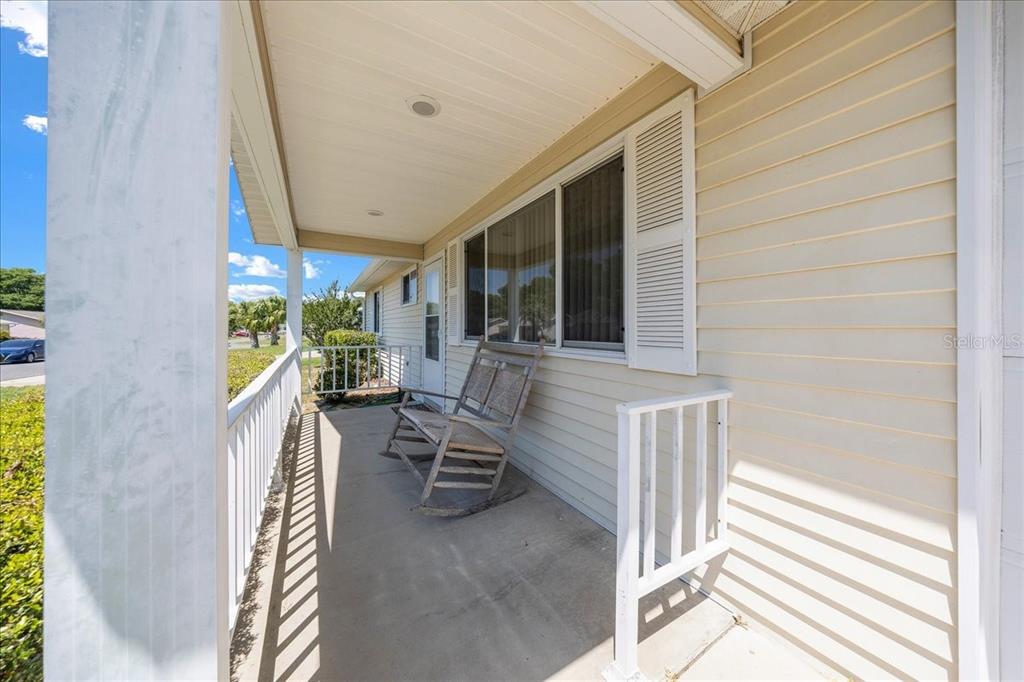A covered front porch features light-colored vinyl siding, a white railing, and a wooden rocking chair — 8445 SW 109TH STREET, OCALA, FL