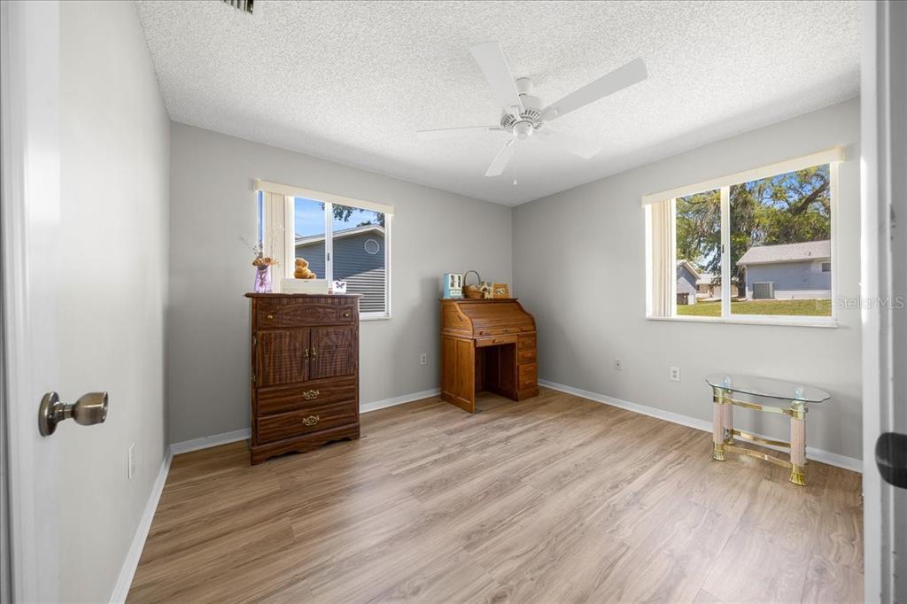 A bedroom with light gray walls, wood-look flooring, a ceiling fan, and two windows — 8445 SW 109TH STREET, OCALA, FL