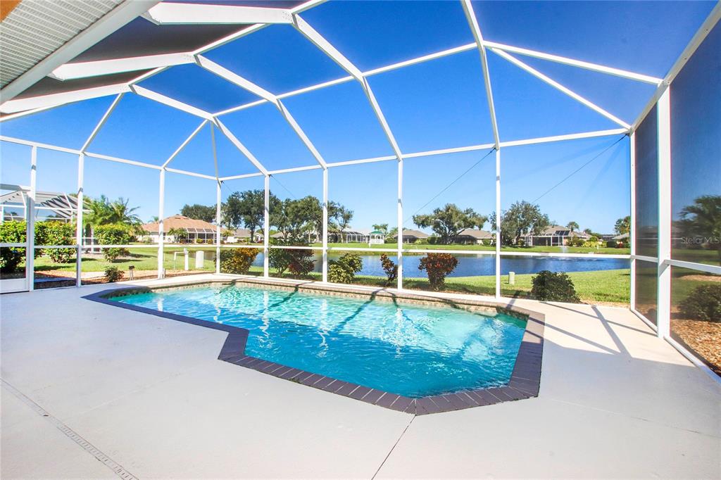 A screened-in swimming pool overlooks a lake with surrounding houses in the distance — 2525 JASMINE WAY, NORTH PORT, FL